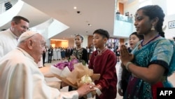 En esta fotografía tomada el 11 de septiembre de 2024 y publicada por Vatican Media, el papa Francisco (izq.) es recibido a su llegada al aeropuerto de Changi en Singapur.