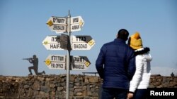 FILE - A couple look towards signs pointing out distances to different cities, on Mount Bental, an observation post in the Israeli-occupied Golan Heights that overlooks the Syrian side of the Quneitra crossing, Israel, Jan. 21, 2019. 