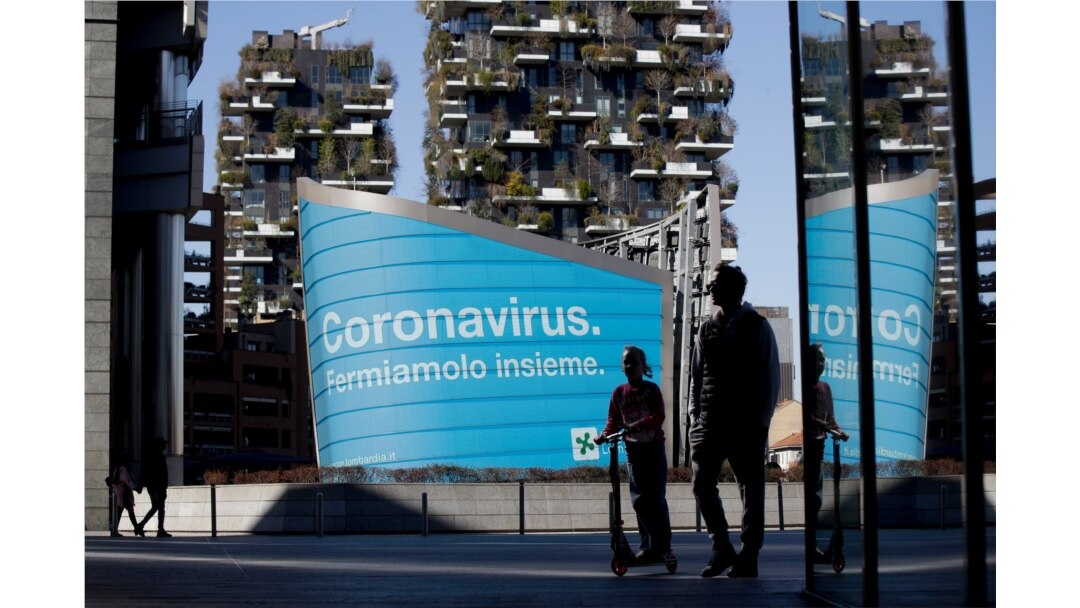A man and a girl on a scooter are backdropped by a Lombardy region campaign advertising reading in Italian "Coronavirus let's stop it together," at the Porta Nuova business district in Milan, March 11, 2020.