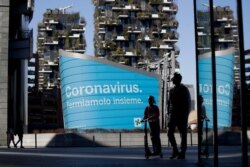 A man and a girl on a scooter are backdropped by a Lombardy region campaign advertising reading in Italian "Coronavirus let's stop it together," at the Porta Nuova business district in Milan, March 11, 2020.