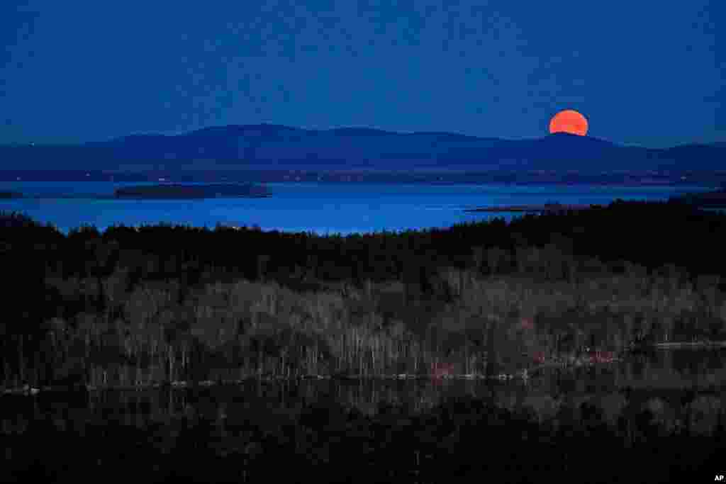 The nearly-full moon sets at dawn behind the Camden Hills in this view looking west across Penobscot Bay, near Camden, Maine.