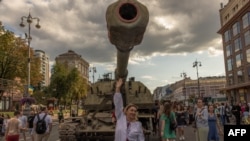 A woman wearing traditional Ukrainian clothes poses for photographs in front of a destroyed Russian armored military vehicle displayed in main street Khreshchatyk Street on Ukraine’s Independence Day in Kyiv, on August 24, 2023. 