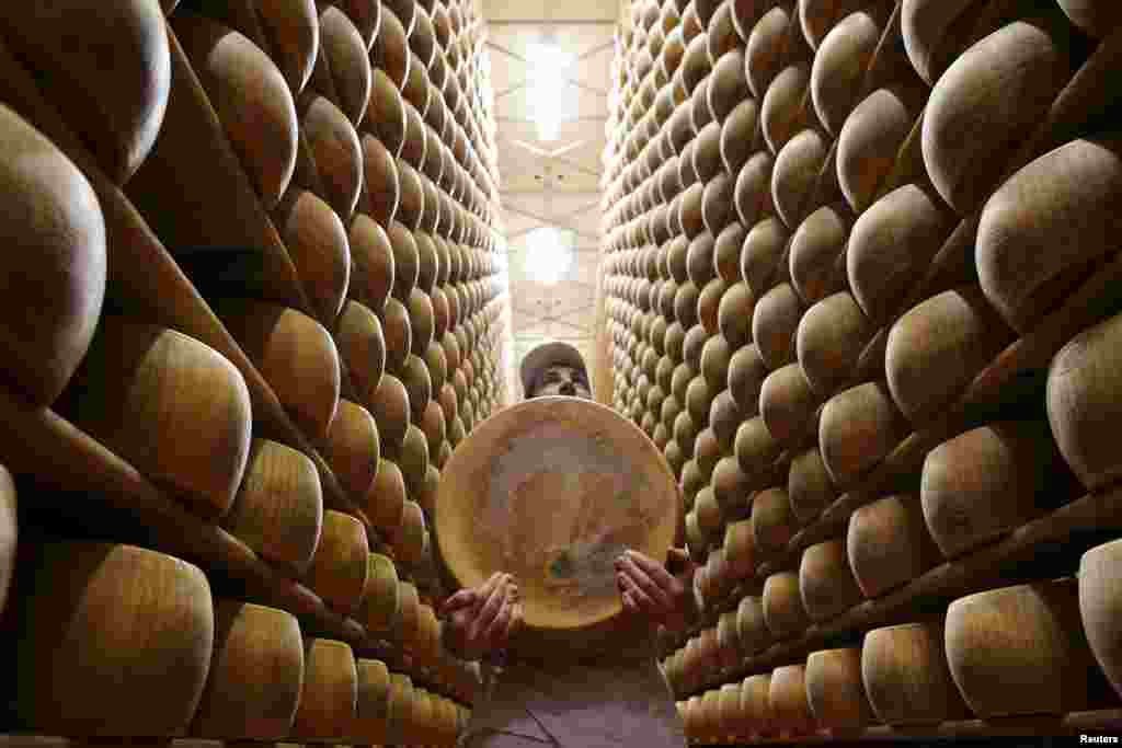 a worker carries a fresh Parmesan wheel off a storehouse shelf at Madonne Caseificio dell&#39;Emilia dairy cooperative in Modena, Italy.