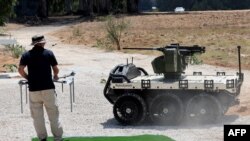 Čovjek stoji u blizini višenamjenskog robotskog bespilotnog zemaljskog vozila ROOK (UGV), razvijenog za nošenje teških tereta i dijela "Legion-X" linije robotskih i autonomnih borbenih rješenja koje proizvodi izraelska međunarodna kompanija za odbrambenu elektroniku