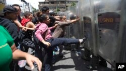 FILE - A woman kicks the shield of a National Guard soldier as other demonstrators push during a protest demanding food, a few blocks from Miraflores presidential palace in Caracas, Venezuela, June 2, 2016.