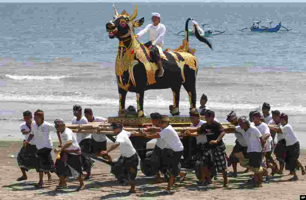 Beberapa pria mengangkat patung sapi dalam sebuah upacara kremasi di sebuah pantai di Bali.