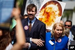 FILE - Dr. Henry Nicholas, left, leads a march with a photo of his sister Marsy Nicholas during the Orange County Victims' Rights March and Rally in Santa Ana, Calif., April 26, 2013. Nicholas is chief architect of Marsy's Law.