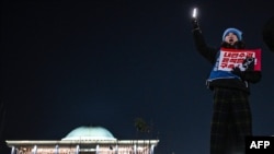 Uma mulher participa num protesto que apela à destituição do Presidente da Coreia do Sul, Yoon Suk Yeol, em frente à Assembleia Nacional, em Seul, a 7 de dezembro de 2024.