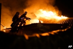 FILE - Firefighters extinguish fire at a house destroyed by night-long shelling in Donetsk, eastern Ukraine, Aug. 16, 2015.