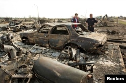 Canadian Prime Minister Justin Trudeau and Fort McMurray Fire Chief Darby Allen, right, look over a burnt out car while visiting neighborhoods devastated by the wildfire that forced the evacuation of the city in Fort McMurray, Alberta, Canada, May 13, 2016.
