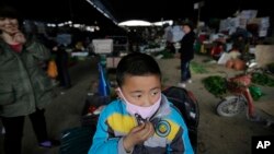 A child wears a mask near the closed poultry section at the Huhai agricultural market where the H7N9 bird flu was detected by authority in Shanghai, China, Apr. 9, 2013. 