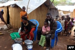 FILE - A family of refugees from the Democratic Republic of Congo sit by their makeshift hut at the Kenani refugee transit camp in Nchelenge, Oct. 30, 2017, during a visit by Zambian President Edward Lungu.