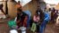 A family of refugees from the Democratic Republic of Congo sit by their makeshift hut at the Kenani refugee transit camp in Nchelenge, Oct. 30, 2017, during a visit by Zambian President Edward Lungu.