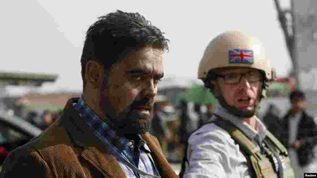 A British security official, right, escorts a survivor from the wreckage of a British embassy vehicle after a suicide attack in Kabul, Afghanistan, Nov. 27, 2014. 