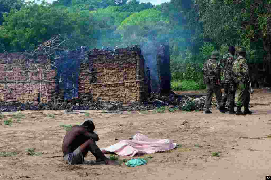 Security officers walk away as a man mourns next to the bodies of his wife and daughter, who were gunned down outside their house as they attempted to escape when suspected Orma raiders attacked their village of Kibusu in Kenya. 