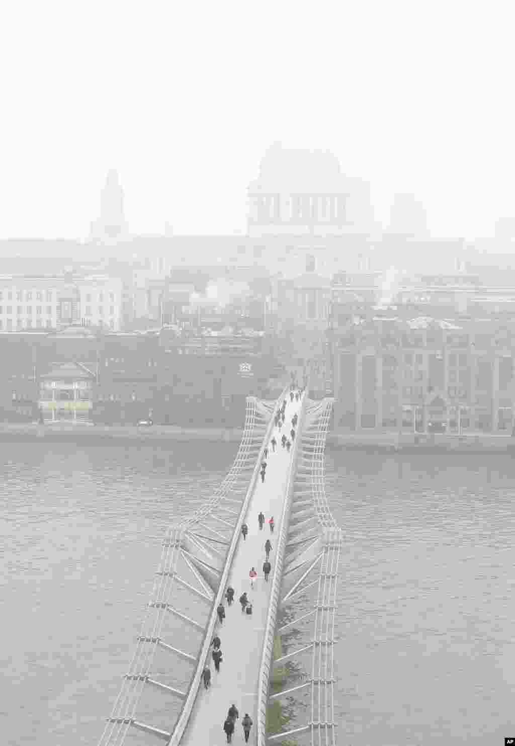 People walk over the Millennium Bridge as fog surrounds St Paul&#39;s Cathedral in London.