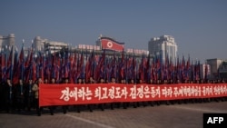 Người dân Triều Tiên cầm bích chương có hàng chữ "Chúng ta hãy hoàn tất lý tưởng của cuộc cách mạnh tự túc (Juche) dưới sự lãnh đạo của Lãnh tụ Tối cao kính yêu Kim Young Un, tại Quảng trường Kim Il Sung, ngày 5/1/2020.