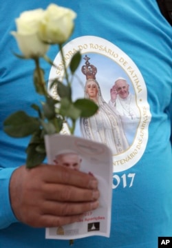 A pilgrim carrying white roses wears a T-shirt with an image of Our Lady of Fatima and Pope Francis at the Fatima Sanctuary, , May 11, 2017, in Fatima, Portugal. Pope Francis is visiting the Fatima shrine May 12-13 to canonize two Portuguese shepherd children.