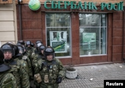 FILE - Interior Ministry security force members stand guard outside a branch of Russian bank Sberbank, which was attacked during a protest against Russia in Kiev, Ukraine, Feb. 20, 2016.
