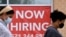 FILE - Women walk past by a 'Now Hiring' sign outside a store in Arlington, Virginia.