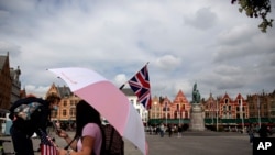 FILE - A tour operator stands under an umbrella with a British and American flag as she waits for customers in the center of Bruges, Belgium, Sept. 2, 2020.