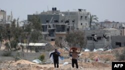 FILE—Men carry heavy items as they walk past damaged buildings in the area around Nasser hospital in Khan Yunis in the southern Gaza Strip on March 24, 2024, as battles continue between Hamas militants and Israeli forces in the besieged Palestinian territory.