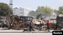 La gente pasa junto a restos de vehículos quemados cerca del palacio presidencial, después de pandillas prendieran fuego, mientras la violencia se extiende y las pandillas armadas amplían su control sobre la capital, Puerto Príncipe, Haití, el 25 de marzo de 2024.