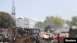 People walk past remains of vehicles near the presidential palace after the cars were set on fire by gangs in Port-au-Prince, Haiti, on March 25, 2024.