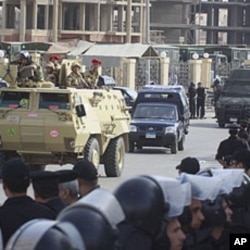 Egyptian policemen line the street as an armored army vehicle guards a convoy carrying former Egyptian interior minister Habib el-Adly and his aides, as they arrive at the court in Cairo, May 21, 2011