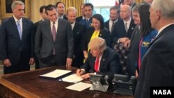 President Donald Trump, center, signs the NASA Transition Authorization Act of 2017, alongside members of the Senate, Congress, and National Aeronautics and Space Administration in the Oval Office of the White House in Washington, Tuesday, March 21, 2017.