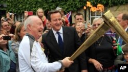 El primer ministro británico David Cameron con el portador de la llama olímica Clive Stone, en Woodstock. Cameron se disculpo por el "error" de confundir la bandera de Corea del Norte.
