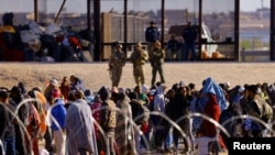 FILE - Migrants stand near the United States/Mexico border wall, as seen from Ciudad Juarez, Mexico. U.S. immigration officials reported more than 2 million migrant encounters along U.S. borders nationwide in fiscal 2022. 