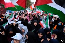 Siswi sekolah Iran mengibarkan bendera Iran dan Palestina saat unjuk rasa di depan bekas Kedutaan Besar AS di Teheran, Iran, memperingati 44 tahun penyitaan kedutaan oleh mahasiswa militan Iran, Sabtu, 4 November 2023. (AP Photo/Vahid Salemi)