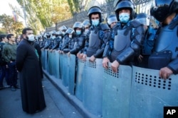An Orthodox priest stands next to police during a protest against an agreement to halt fighting over the Nagorno-Karabakh region, in Yerevan, Armenia, Nov. 11, 2020.