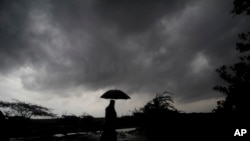 FILE - A villager holds an umbrella as dark clouds loom over Balasore district, in India, May 25, 2021, ahead of a powerful storm. When it comes to measuring global warming, it’s not just the heat, it’s the humidity that matters in climate extremes.