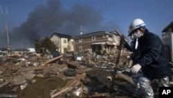 A body, covered in a blanket, lies in the rubble of a destroyed neighborhood as firefighters search the area in Sendai, Miyagi Prefecture, northeastern Japan, two days after a giant quake and tsunami struck the country's northeastern coast, March 13, 2011