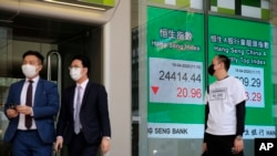 People wearing face masks walk past an electronic board showing Hong Kong share index outside a local bank in Hong Kong, Wednesday, April 15, 2020. 