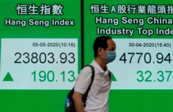 A man wearing face mask walks past a bank electronic board showing the Hong Kong share index Tuesday, May 5, 2020.