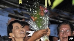 Burma's pro-democracy leader Aung San Suu Kyi smiles after she received flowers from her supporters as she stands at the gate of her home in Rangoon, 13 Nov 2010