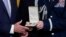 FILE - A military aide hands a Presidential Citizens Medal, the nation's second-highest civilian honor, to President Joe Biden during a ceremony in the East Room of the White House in Washington, Jan. 6, 2023. 