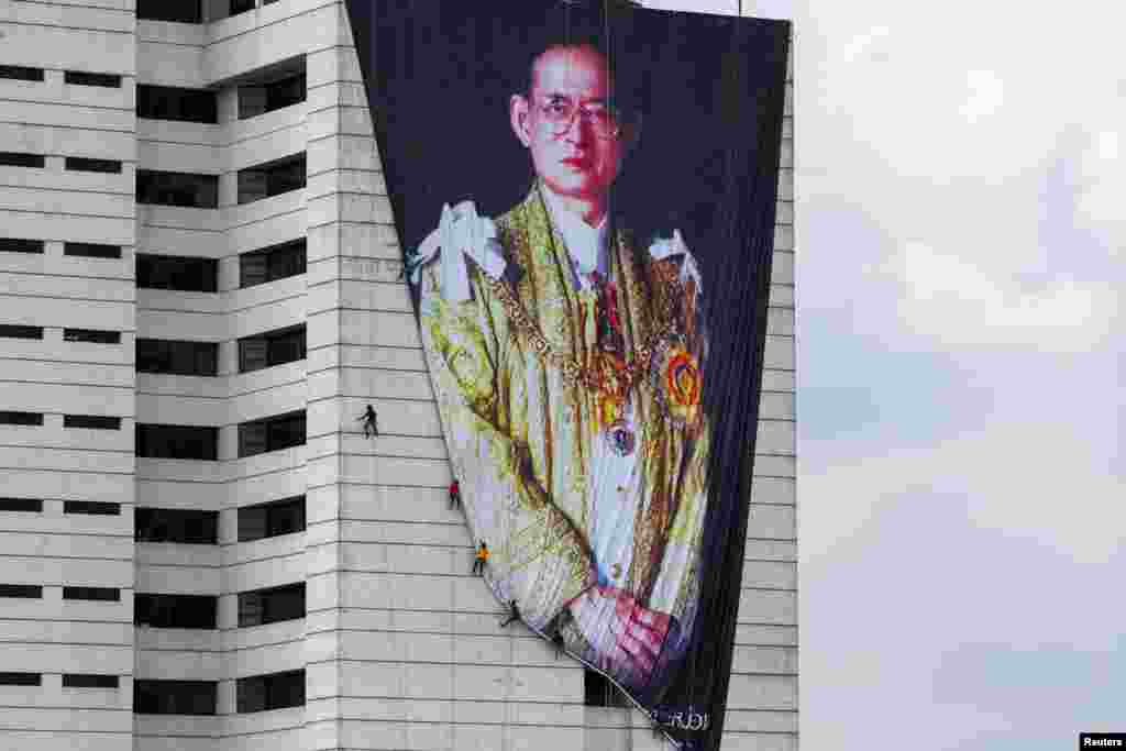 Workers install a portrait of Thailand's late King Bhumibol Adulyadej at a building in Bangkok.