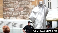 BOSNIA-HERZEGOVINA -- A police officer stands next to a statue of Pope John Paul II in front of the Catholic Cathedral in Sarajevo, May 14, 2020