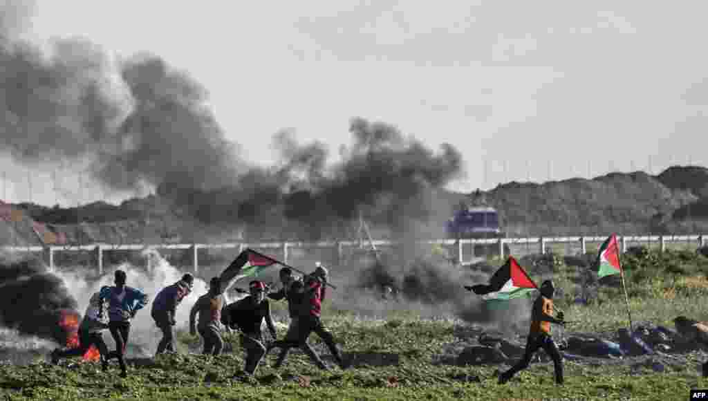 Palestinian protesters holding national flags walk past burning tires during a demonstration near the fence along the border with Israel, east of Gaza City.