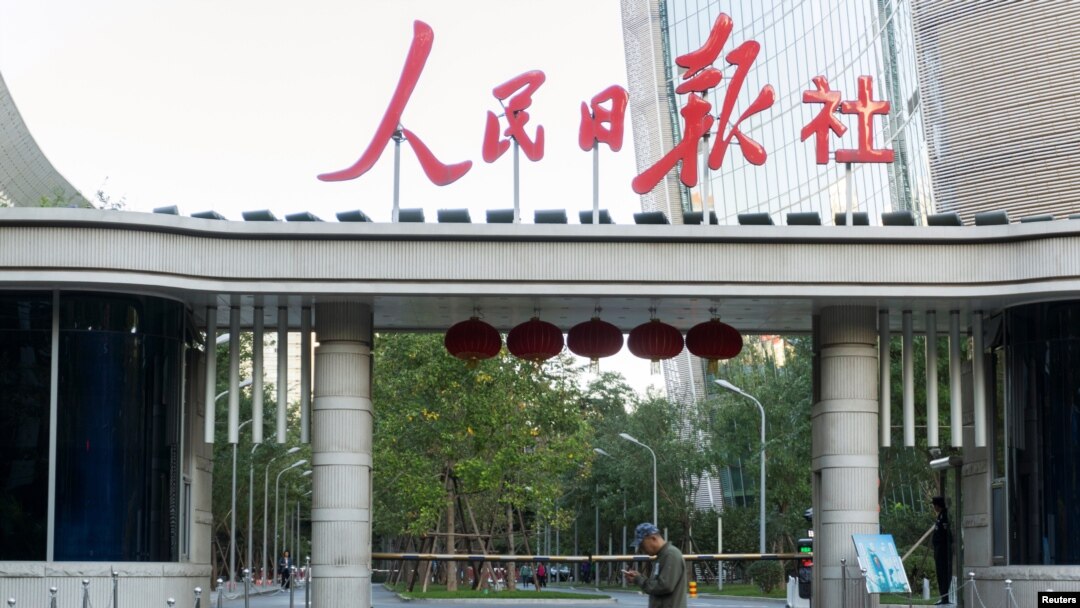 FILE - A man holding a smartphone walks past the headquarters of the Chinese Communist Party newspaper People's Daily, in Beijing, China, Oct. 6, 2018. 