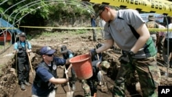 Bob Wood, Garden Valley, Calif., a members of the JPAC, Joint POW/MIA Accounting Command, second from left, deliveries a basket containing earth to South Korean Army soldiers Lee Byung-jin as he digs to search for remains of U.S. soldiers killed during the 1950-53 Korean War in Hwacheon, South Korea, May 18, 2009. 