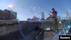 Kurth Reis is seen through a giant bubble he made on a rooftop in San Francisco, California. He makes bubbles by dipping his long sticks connected by small ropes into a mixture. (REUTERS/Nathan Frandino)