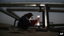 An oil field employee welds a pipeline in the desert oil fields of Sakhir, Bahrain at sunset, June 10, 2014. 