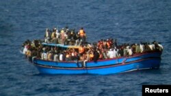 FILE - Migrants sit in their boat during a rescue operation by Italian navy ship Grecale (not pictured) off the coast of Sicily.