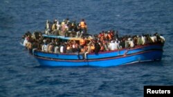 Migrants sit in their boat during a rescue operation by Italian navy ship Grecale (not pictured) off the coast of Sicily, in this handout picture by the Italian Marina Militare, June 29, 2014.