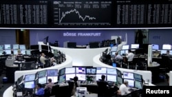 FILE - Traders are pictured at their desks in front of the DAX board at the stock exchange in Frankfurt, Germany, Aug. 21, 2015. 